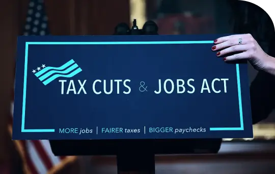 Hand holding 'TAX CUTS &amp; JOBS ACT' sign. Aims: 'MORE jobs | FAIRER taxes | BIGGER paychecks'. Boosts economy and reg cf investment.